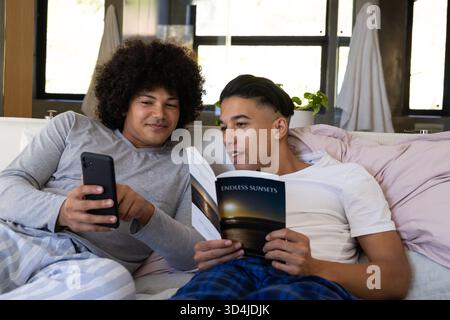 Se prélasser divers amis masculins lisant des couchers de soleil sans fin et vérifiant smartphone sur le lit avec couverture Banque D'Images
