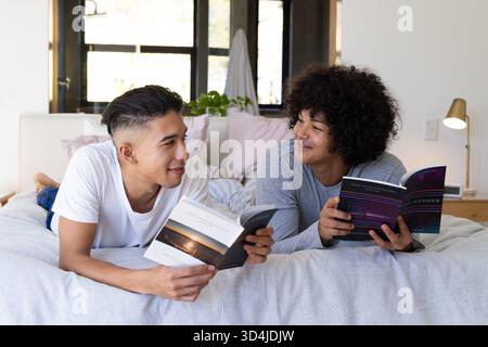 Lecture de divers amis masculins allongés sur le lit dans une chambre confortable, avec livres de poche et lumière naturelle Banque D'Images