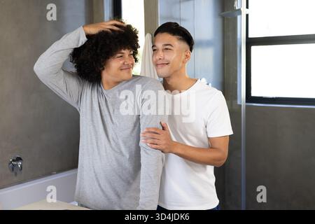 Souriant divers partenaires masculins debout près les uns des autres à l'évier de salle de bain moderne, avec miroir mural Banque D'Images