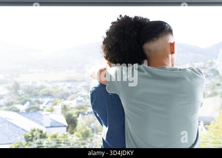 Embrassant divers partenaires masculins debout à l'intérieur à grande fenêtre, capturant la vue ensoleillée sur la colline Banque D'Images