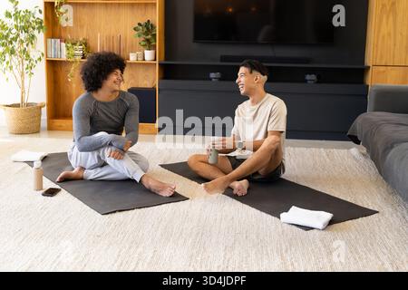 Discuter divers amis masculins assis sur des tapis de yoga dans un salon lumineux, tenant des bouteilles d'eau Banque D'Images