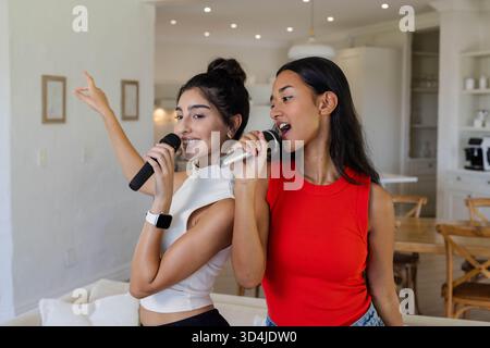 Chanter diverses amies se tenant dos à dos à la maison, avec des microphones sans fil Banque D'Images