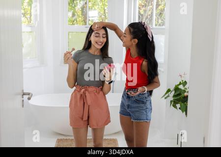 Souriant diverses amies féminines appliquant le maquillage dans la salle de bains à la maison, avec pinceau de maquillage et palette Banque D'Images