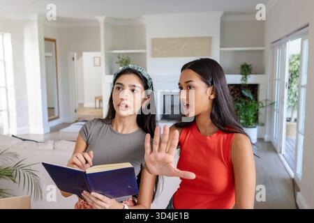 Diverses amies féminines collaborant sur le plan du projet dans le salon à la cheminée, tenant un cahier Banque D'Images