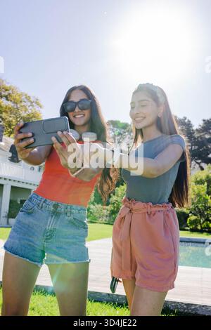 Prise de selfie, diverses amies féminines posant dans la cour près de la piscine avec téléphone, montre et écouteurs Banque D'Images