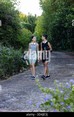 Marchant diverses amies féminines discutant sur le chemin du jardin, avec des tapis de yoga et des bouteilles d'eau Banque D'Images