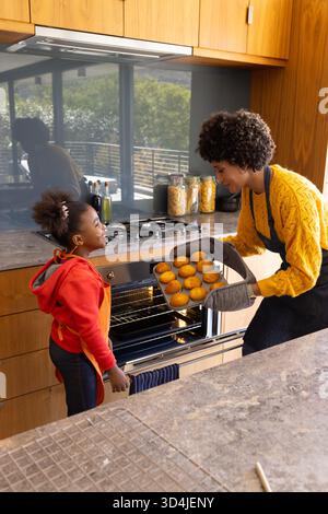 Cuisson de divers mères et filles tenant plateau de brioches dorées dans la cuisine à la maison, avec four ouvert Banque D'Images