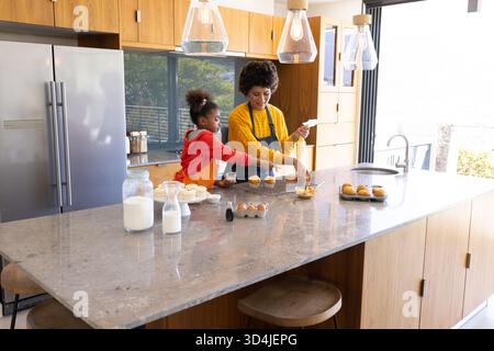 Mélange diversifié mère et fille préparant la pâte à cupcake à l'îlot de cuisine, avec bol à mélanger Banque D'Images
