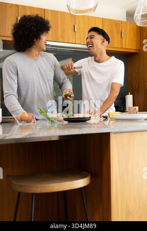 Cuisiner divers amis masculins tranchant l'avocat sur l'île de marbre dans la cuisine moderne, avec planche à découper Banque D'Images
