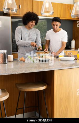 Hacher des légumes divers amis masculins préparant le repas à l'îlot de cuisine, avec de l'avocat et des épices Banque D'Images