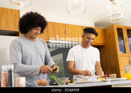 Divers amis masculins coupant l'avocat et tranchant le pain à l'îlot de cuisine, avec des ingrédients frais Banque D'Images