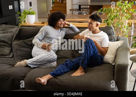 Siroter du café divers amis masculins se détendre sur le canapé sectionnel dans le salon, avec des plantes en pot Banque D'Images