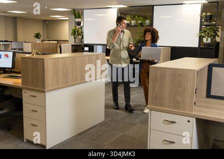 Collaborer avec divers collègues pour discuter des plans de projet dans un bureau ouvert, avec un ordinateur portable et un tableau blanc Banque D'Images