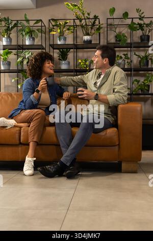 Bavardez divers amis assis sur le canapé en cuir dans le salon, avec des tasses à café et des plantes sur les étagères Banque D'Images
