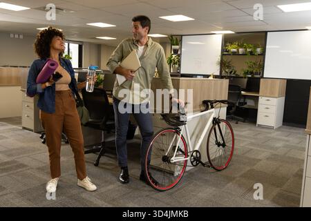 Marcher divers collègues parlant près des cabines dans un bureau ouvert, avec tapis de yoga et vélo Banque D'Images