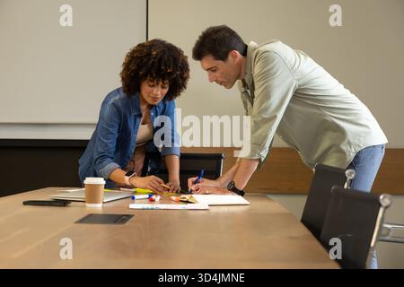 Penchant divers collègues esquissant sur du papier dans la salle de conférence de bureau, avec des marqueurs et une tasse à café Banque D'Images