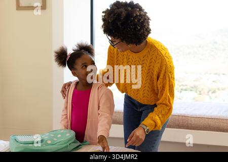 Mère et fille diversifiées discutant des travaux scolaires à la table à manger, avec sac à dos à pois sarcelle Banque D'Images