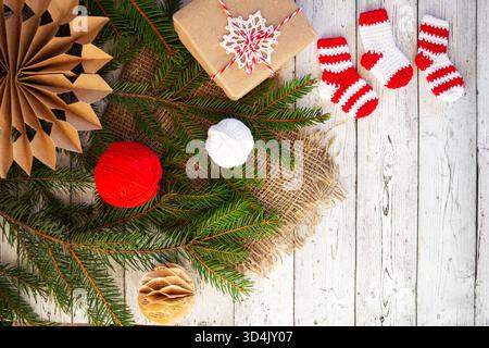 Chaussettes mignonnes crochetantes rouges et blanches faites à la main avec le thème de Noël sur fond de bois rustique avec des branches de sapin, des boules de fil et un emballage cadeau artisanal. Banque D'Images
