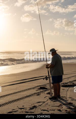 Les pêcheurs tôt le matin jettent des lignes au lever du soleil sur la côte de Floride, debout près de l'océan Atlantique dans une douce lumière dorée. Scène côtière paisible Banque D'Images