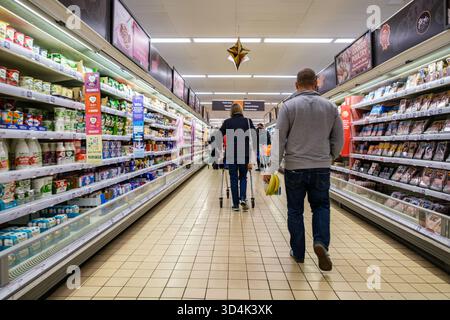 Londres Royaume-Uni, 10 novembre 2025, homme marchant vers le bas de l'allée du supermarché transportant des bananes en bouquet Banque D'Images
