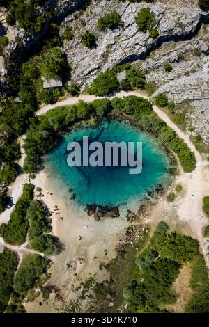 La vue aérienne d'un œil bleu profond fascinant de la source de la rivière Cetina contraste radicalement avec le paysage rocheux environnant, Cetina, Croatie. Banque D'Images