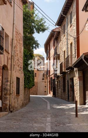 Une étroite rue pavée serpente à travers un village pittoresque. Le soleil brille brillamment, éclairant les bâtiments rustiques et la verdure luxuriante dans le b. Banque D'Images