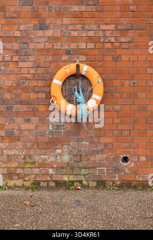 Anneau de bouée de sauvetage orange brillant monté sur le mur de briques avec corde et sol altéré Banque D'Images