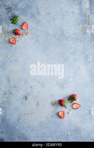 Photographie culinaire minimaliste de fraises fraîches et flocons de muesli dispersés sur une surface bleue texturée. Parfait pour illustrer un petit déjeuner sain Banque D'Images