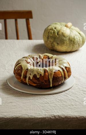 gâteau bundt à la citrouille en marbre avec glaçage blanc sur une assiette, placé sur une nappe de lin avec une citrouille rustique en arrière-plan Banque D'Images