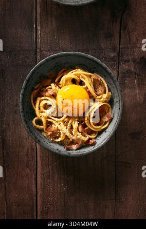 vue de dessus d'un plat unique de pâtes carbonara avec jaune d'oeuf cru au milieu avec fromage pecorino et guanciale (bacon) sur une table en bois Banque D'Images