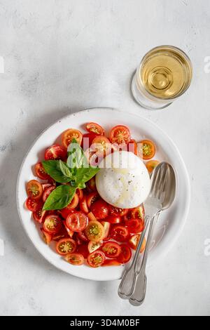 Assiette avec des tomates cerises, une mozzarella au centre et un petit bouquet de basilic vert vif, le tout sur fond clair. Vue de dessus. Banque D'Images