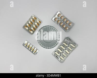 Il s'agit d'une photo plate ou top-down montrant un petit verre d'eau entouré de quatre blisters différents de pilules ou de capsules Banque D'Images