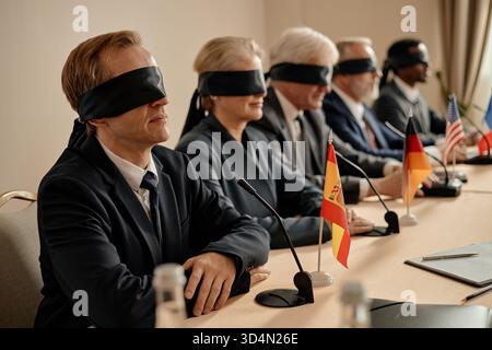 Groupe de gens d'affaires multiethniques d'âge moyen assis les yeux bandés à la conférence Banque D'Images