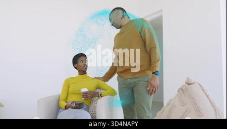 Femme assise en haut jaune, homme debout en pull moutarde penché dans le salon, tenant le téléphone Banque D'Images