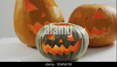 Citrouille sculptée vert-gris éclatante assise sur une table blanche dans le studio, avec deux citrouilles orange allumées Banque D'Images