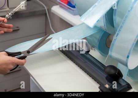 Un professionnel de la santé utilise une machine de thermoscellage constante pour créer des sachets de stérilisation pour les instruments dentaires dans une clinique ou un laboratoire propre et moderne Banque D'Images