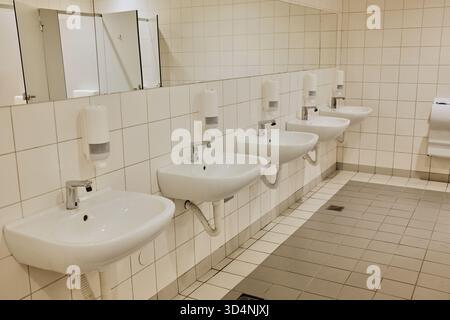 Toilettes modernes dans le centre commercial avec plusieurs lavabos blancs, miroirs et murs carrelés. Le concept met l'accent sur l'hygiène, la propreté et l'ordre. Banque D'Images