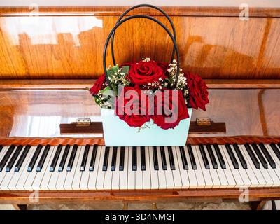 bouquet de roses rouges fraîches dans la boîte de sac sur le clavier du piano verni en bois Banque D'Images