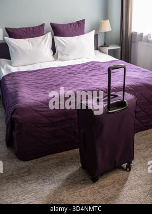 valise de voyage violette et lit double avec draps blancs et couvre-lits violets, avec oreillers blancs et violets dans le petit salon Banque D'Images