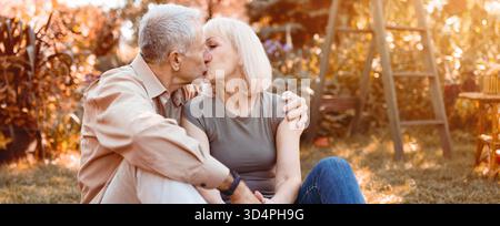 Couple âgé partage un baiser tendre dans un jardin ensoleillé pendant l'automne Banque D'Images