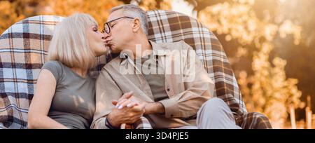 Couple de personnes âgées partage un baiser tendre dans un cadre de plein air confortable pendant Golden Hour Banque D'Images