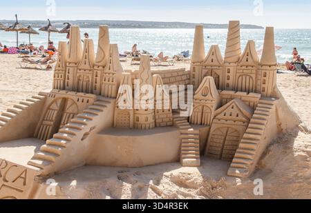 Grande sculpture complexe de château de sable avec des tours et des escaliers sur une plage bondée près de la mer Banque D'Images