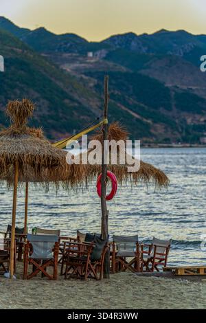 Chaises de plage vides et parasols en paille près du lac au coucher du soleil Banque D'Images
