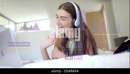 Agitant femme couchée dans la chambre portant le dessus sans manches, casque, en utilisant un ordinateur portable avec des graphiques de données Banque D'Images