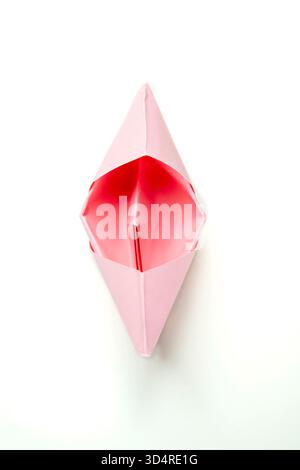 Bateau en papier rose isolé sur un fond blanc. Concept de voyage, d'exploration et de navigation Banque D'Images