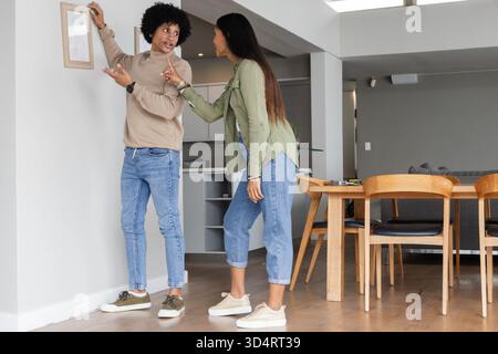 Accrocher le cadre photo de positionnement de couple diversifié sur le mur moderne du salon, avec table en bois Banque D'Images