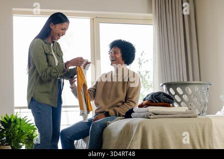 Linge pliant de couple diversifié dans une chambre lumineuse par fenêtre, avec panier à linge et vêtements pliés Banque D'Images