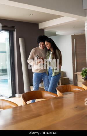 Vérification smartphone, couple diversifié debout dans la salle à manger moderne à la maison, avec des boîtes mobiles Banque D'Images