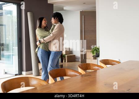 Embrassant un couple diversifié s'installant dans une maison ouverte, avec des boîtes mobiles et une table, un espace de copie Banque D'Images