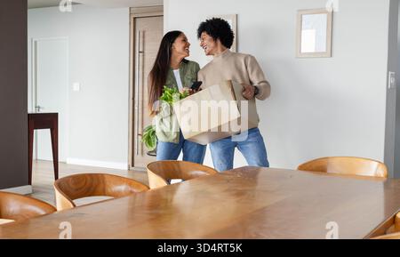 Transporter la boîte mobile à l'entrée par la table à manger, couple diversifié tenant smartphone et plante Banque D'Images